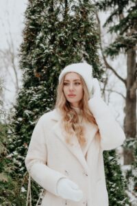 Stylish woman in winter attire posing amidst snow-covered trees.