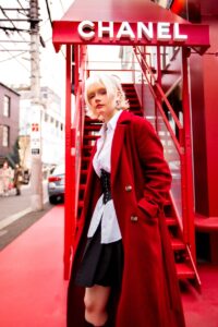 Fashionable woman in a red coat posing outside a Chanel store in an urban setting.